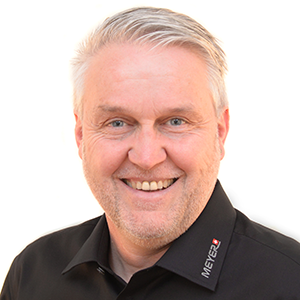 Lächelnder Mann mittleren Alters, graue Haare, schwarze MEYER-Arbeitskleidung, Experte für Schutzeinrichtungen Arbeitsschutz.