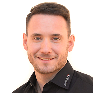 Luigi Gojani mit kurzem braunen Haar, Bart, im MEYER-Shirt für Arbeitsschutztechnik, lacht vor weißem Hintergrund.