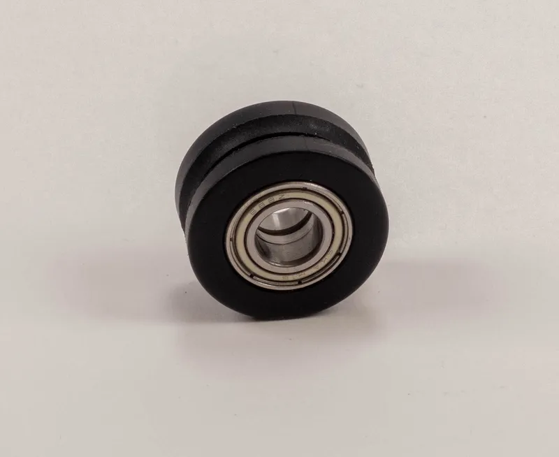 Schwarze Kunststoff-Laufrolle für Messerwellenabdeckung (319), zentralem Kugellager, stehend auf hellem Untergrund.