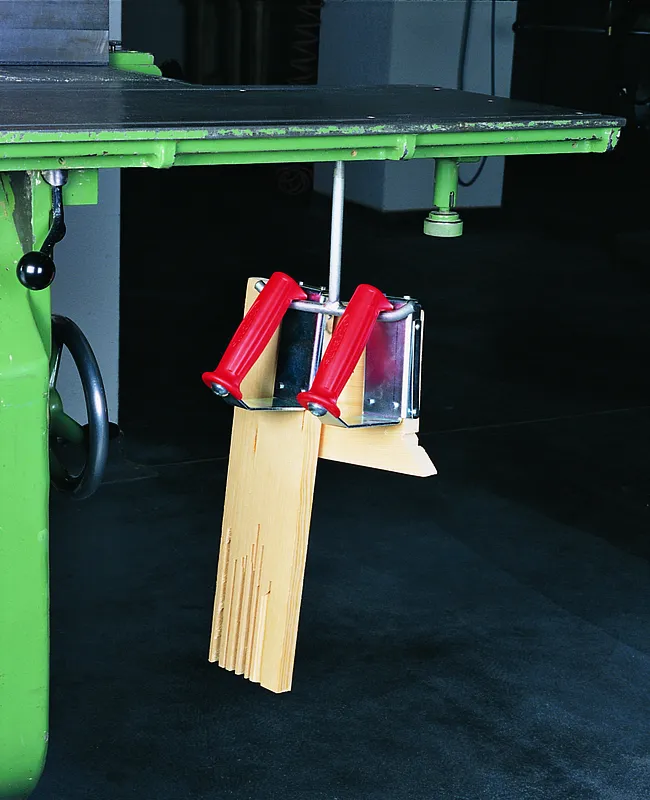 Ein Doppelhaken für Handgriffe (605) ist umgekehrt am Tisch fixiert und hält ein Brett mit mehreren schmalen Nuten.