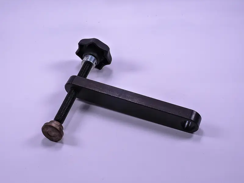 Klemmvorrichtung, Ausladung 140 mm, Metall, schwarzer Griff, Gewindespindel, Druckplatte auf hellem violettem Untergrund.