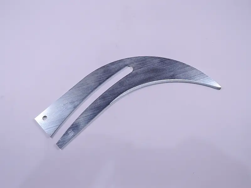 Ein Spaltkeil 350x3,2 mm und ein gebogenes Metallteil liegen auf violettem Untergrund; eines mit Loch und Langschlitz.