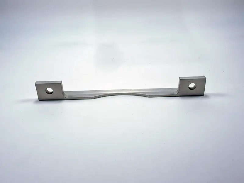Ein flaches Anschlaglineal aus Metall, 195 × 3 mm, mit zwei rechten Winkeln und Bohrungen, liegt auf hellem Hintergrund.