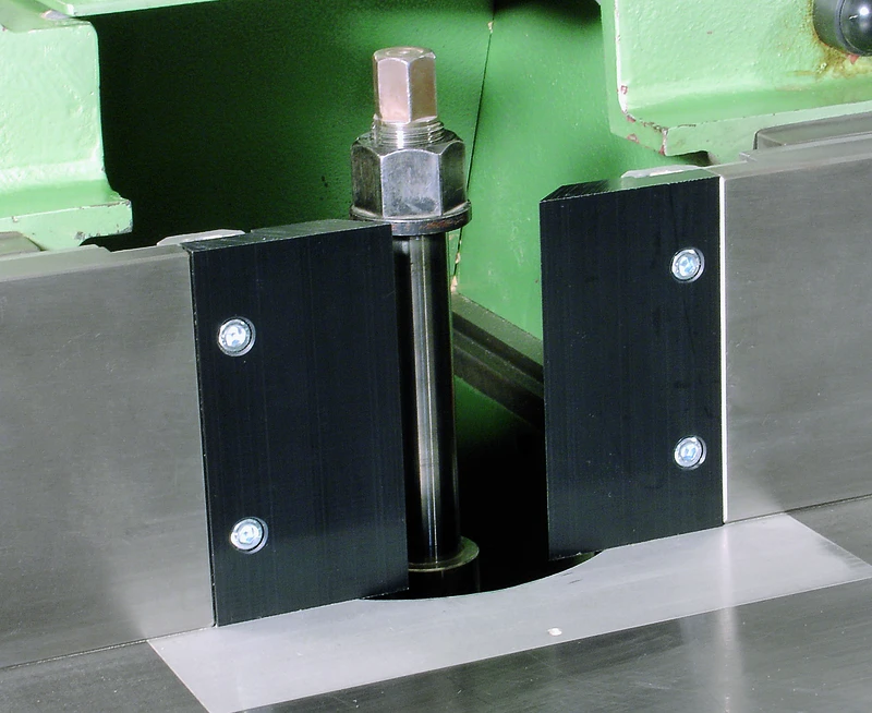 Detailaufnahme Maschinenbauteil mit senkrechter Stange, Schutzabdeckung, Schrauben und Anschlaglippe 150x80mm im Hintergrund.
