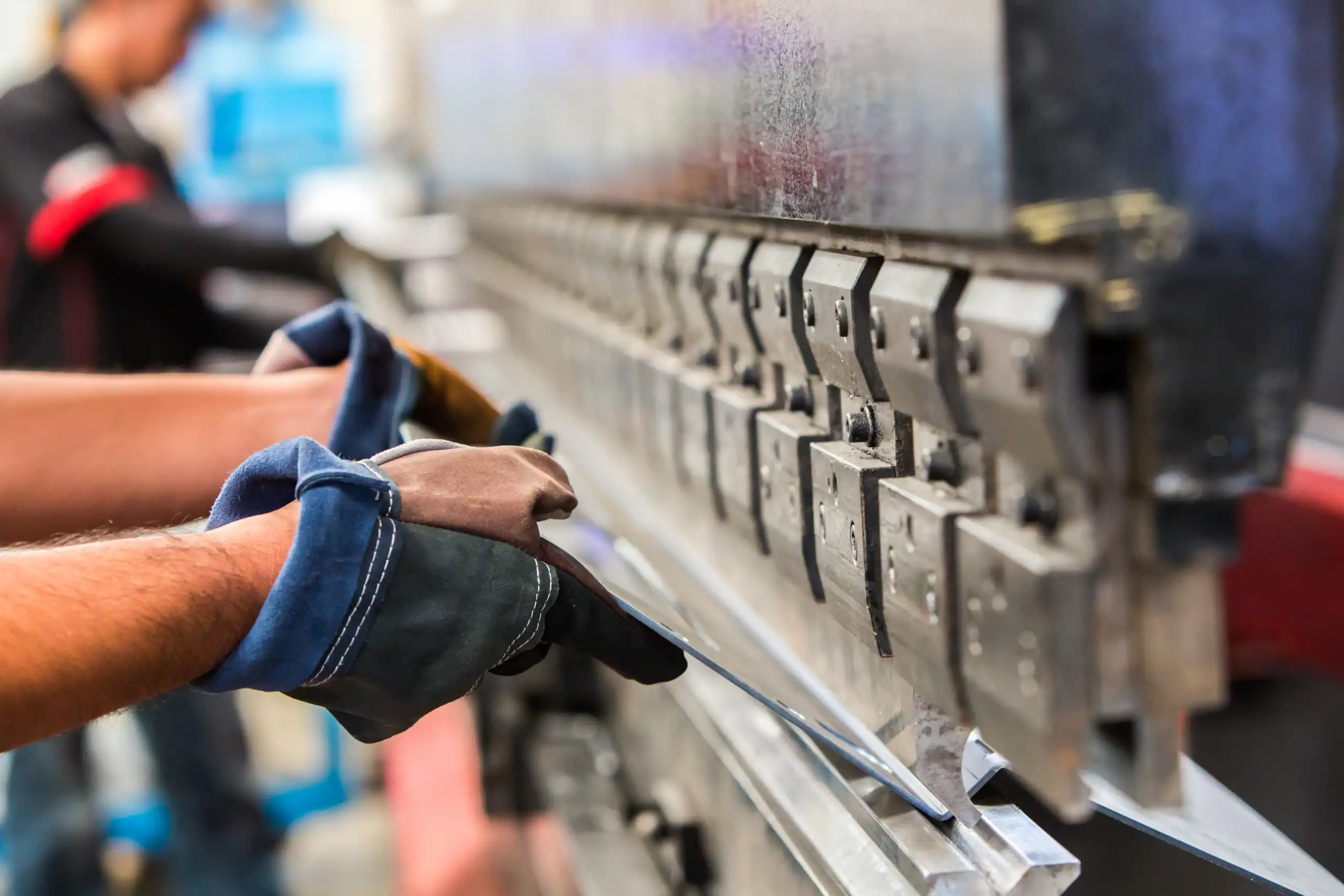 Ein Monteur mit Schutzhandschuhen bedient eine Biegemaschine, sichert das Metall mit Schutzvorrichtung für Arbeitssicherheit.