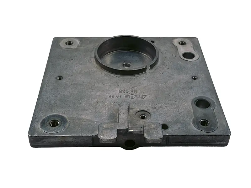 Die Führungsplatte 308 ist eine quadratische Metallplatte mit Bohrungen, Nuten und erhöhter Mittelachse, auf Weiss.